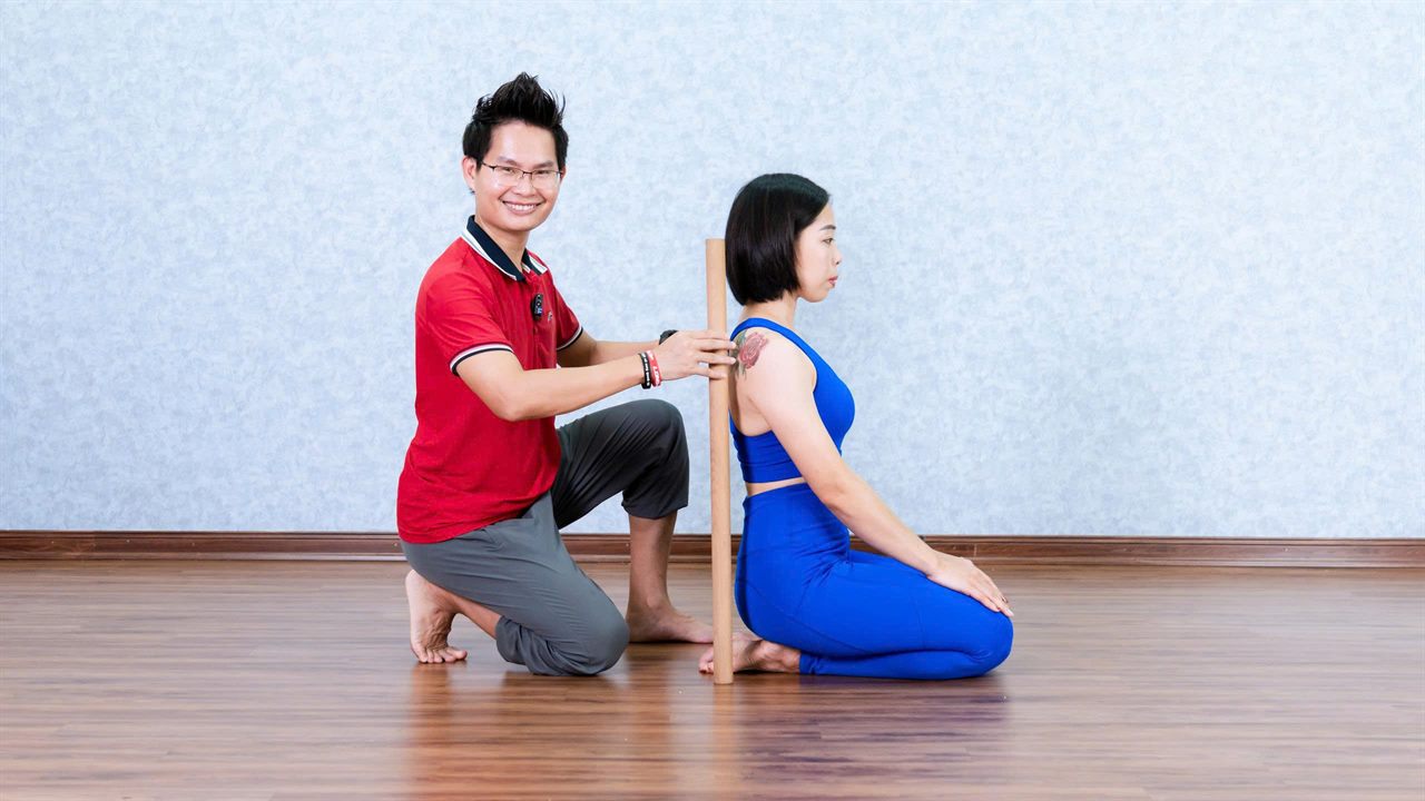 5 Kiểu Căng Cứng Khiến Bạn Tập Yoga Nhiều Năm Vẫn Không Dẻo 7 Đặng Kim Ba dùng gậy định tuyến căn chỉnh trục cột sống thẳng cho học viên trong buổi tập Yoga phục hồi tại Học viện Yoga T.Kim