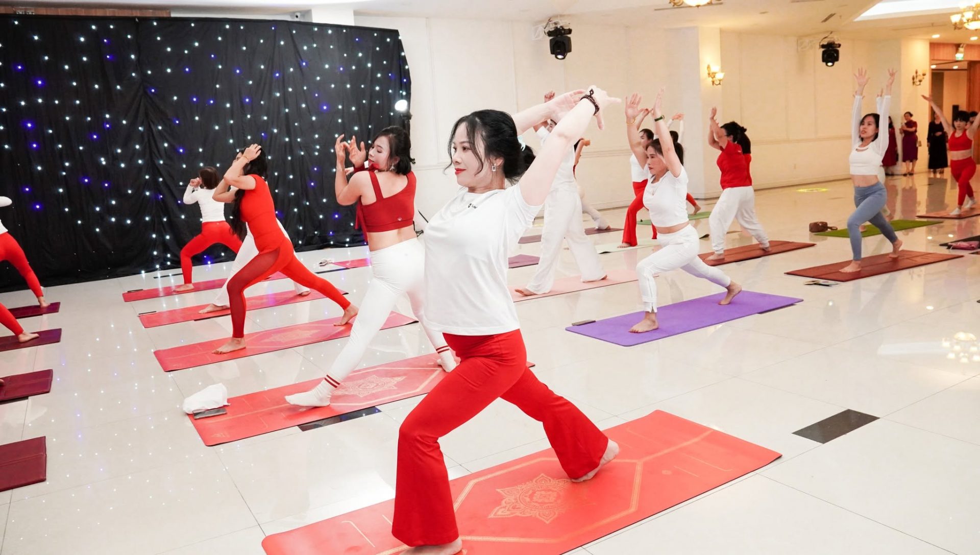 Phía Sau Mỗi Học Viên Là Một HLV Chăm Sóc Riêng — Câu Chuyện Thanh Hương T.Kim Yoga 7 Trần Thanh Hương cùng đội ngũ học viên Học viện Yoga T.Kim Việt Nam tham dự sự kiện cộng đồng Yoga Dẫn Lối Nét Đẹp Việt — đồng phục đỏ trắng trong tư thế chiến binh