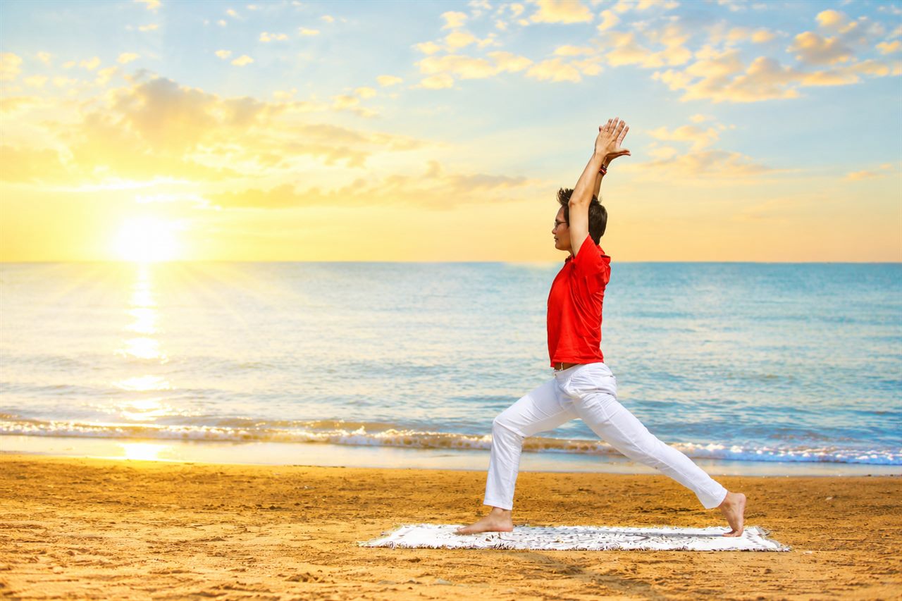 Yoga Buổi Sáng: Vì Sao Tập Sớm Tốt Cho Tim Mạch Hơn? Góc Nhìn Khoa Học 8 Người tập Yoga tư thế chiến binh hướng về phía mặt trời mọc trên bãi biển buổi sáng - Yoga đón ngày mới